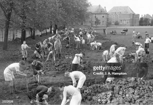 Pupils at Harrow School dig air raid precaution trenches under the supervision of their masters, in the school playing field. The trenches will...