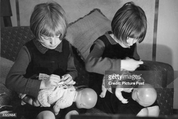 Two little girls sitting on a couch dressing their dolls. Original Publication: Picture Post - 1448 - What It Means To Live In A Not So Good House -...
