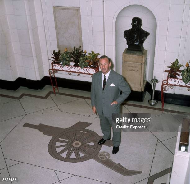 Arsenal Football Club manager Bertie Mee standing in front of a bust of a former manager, Herbert Chapman, with the team's 'Gunners' cannon logo...