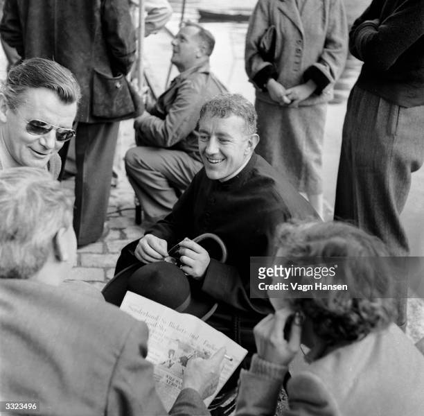 British actor Alec Guinness talks to locals whilst on location in Paris for the filming of 'Father Brown', in which he plays G K Chesterton's famous...