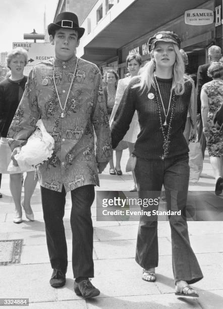 Young couple dressed in hippy clothes walk down a London road.