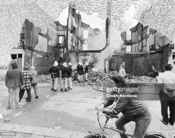 Firemen and onlookers beside a burnt-out building on the second day of riots in Brixton, South London, 13th April 1981.