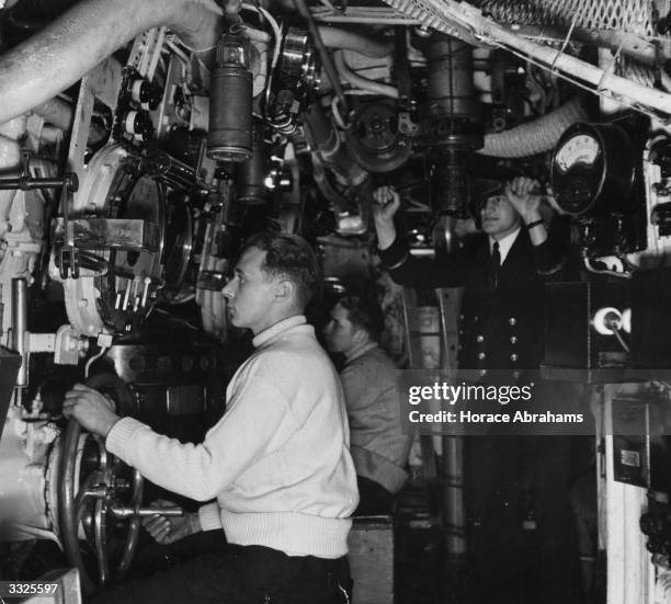 The Commander looks through the periscope and a rating watches the depth gauge in the control room of a submarine as it is diving.