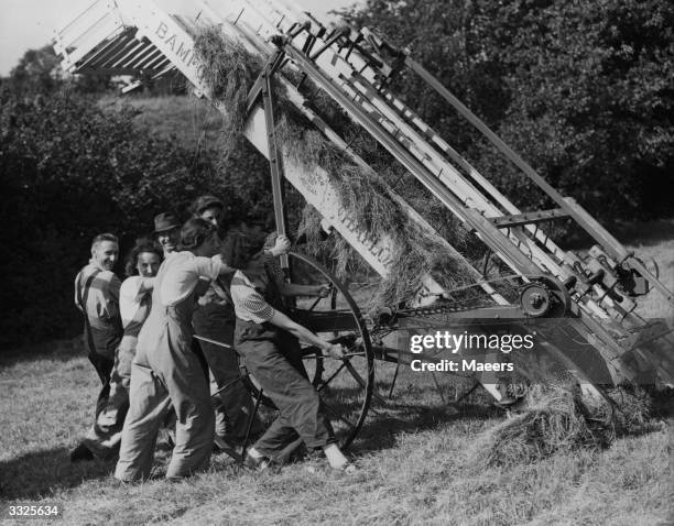 Land girls helping manhandle a hay baler at harvest time.