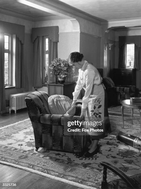 Woman wearing a patterned apron cleaning an armchair with a vacuum cleaner.