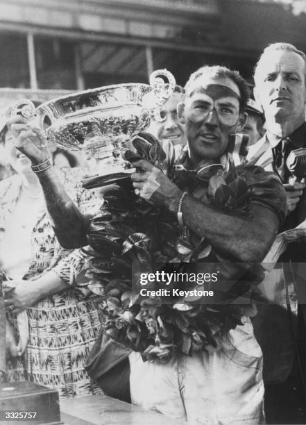 English motor-racing driver Stirling Moss, the winner's laurels around his neck, holds up the Grand Prix Cup after winning the British Grand Prix at...