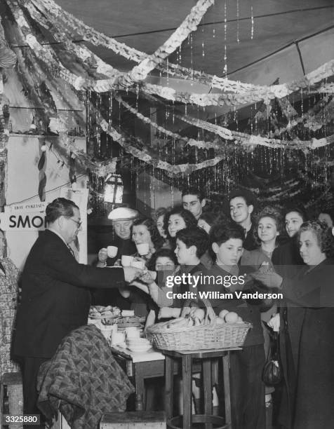 The occupants of a beautifully decorated London bomb shelter enjoying refreshments, after working day and night to give their refuge a Christmas...