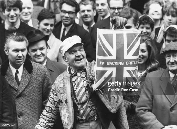 An optimistic member of the British public holding up a plastic carrier bag declaring 'I'm Backing Britain', as he waits for the Chancellor of the...