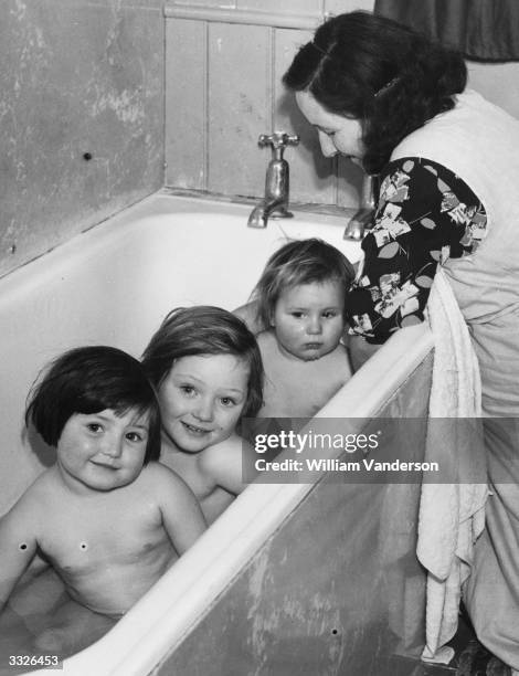 Evacuated mother Mrs Gwendoline Cook of Mitcham, Surrey, bathes her three children in the bathroom at Stone Hall Mansion, the country house of Lady...