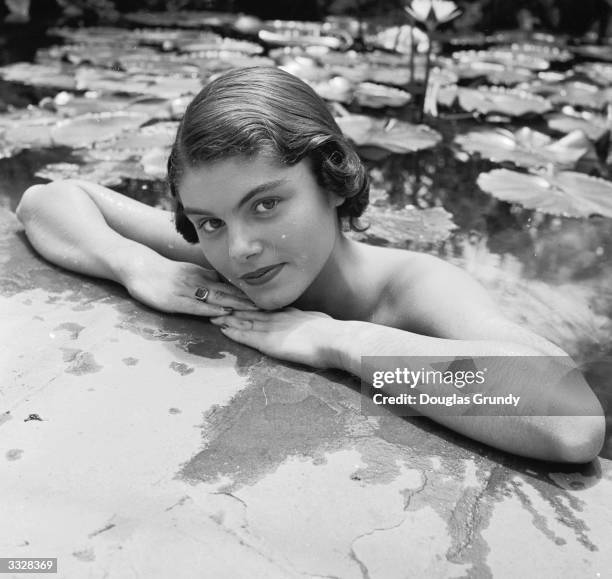 Young women in a water lily pond rests her arms on the edge as she catches the photographer's eye.