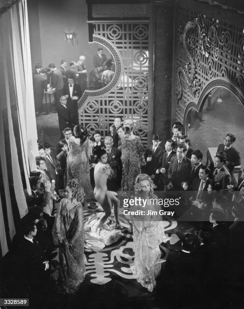 Actor Gregory Peck stands in the background as a scene from the film 'Chairman' is being shot at Pinewood Studios. The film concerns Hong Kong strip...