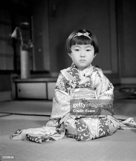 Child wearing a typical Japanase Geisha kimono sits in a Geisha pose.