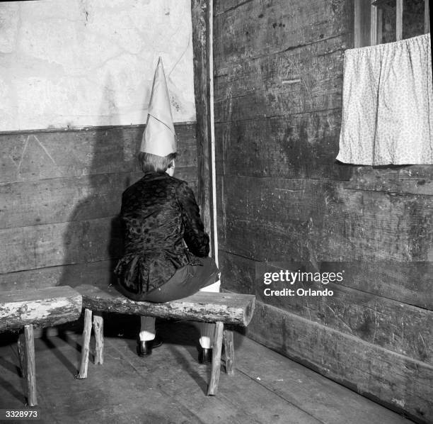 Naughty child sits in the corner and wears the dunce's cap, in a reconstruction of the old teaching methods and conditions at a one-room school in...