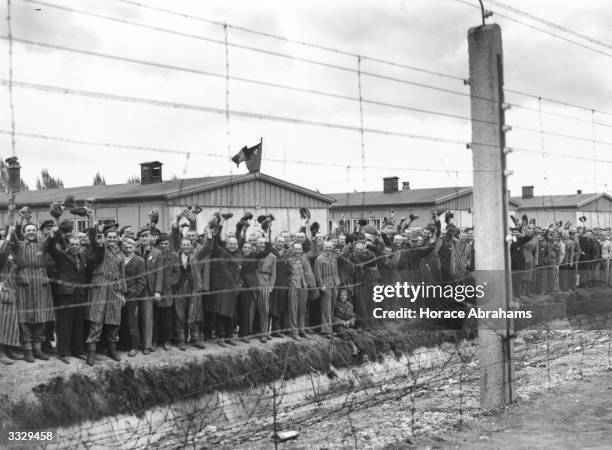 Prisoners behind the electric fence at Dachau concentration camp cheer the US troops who liberated the camp. Some of the prisoners are wearing...