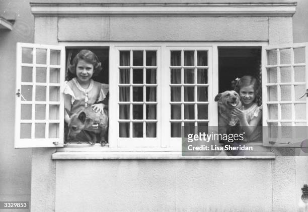 The Royal Princesses Elizabeth and Margaret at the windows of the Royal Welsh House with two Corgi dogs, June 1936.
