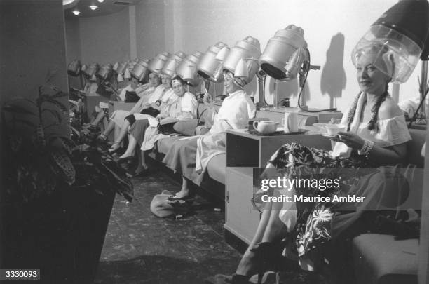 Frances Day and a group of women enjoying a cup of tea whilst sitting under the hairdryers at the Martin Douglas and Rene hair salon. Original...