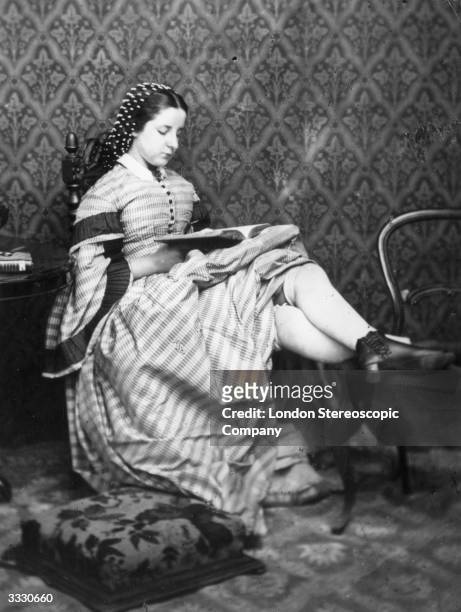 Victorian girl reads a book, her skirts hitched up to show her thick, knee length stockings. London Stereoscopic Company Comic Series