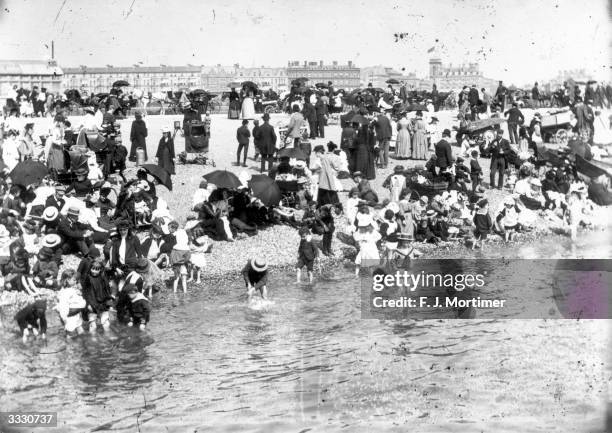 Stony and crowded beach at Southsea, a few children are paddling.