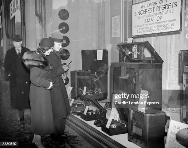 Couple look in to a shop window containing 'HMV' televisions and radios.