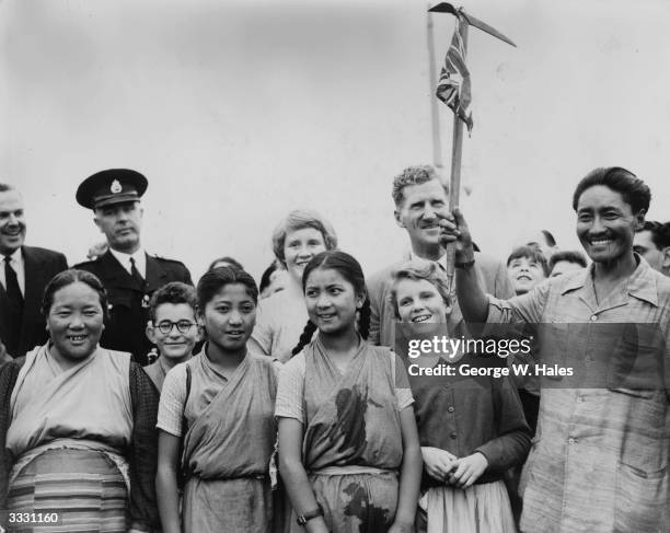 Sherpa Tensing waving an ice-pick with a Union Jack tied to it when he arrived at London Airport after his successful ascent of Everest. Behind him...