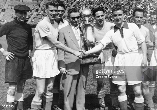 Jack Flamhaft, President of the American Soccer League, holds the Lewis Cup before the final. Players from the teams competing for the trophy stand...