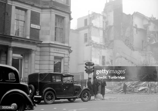 Two models wearing fashion by Molyneux stand in a London street with a bomb-site in the background.