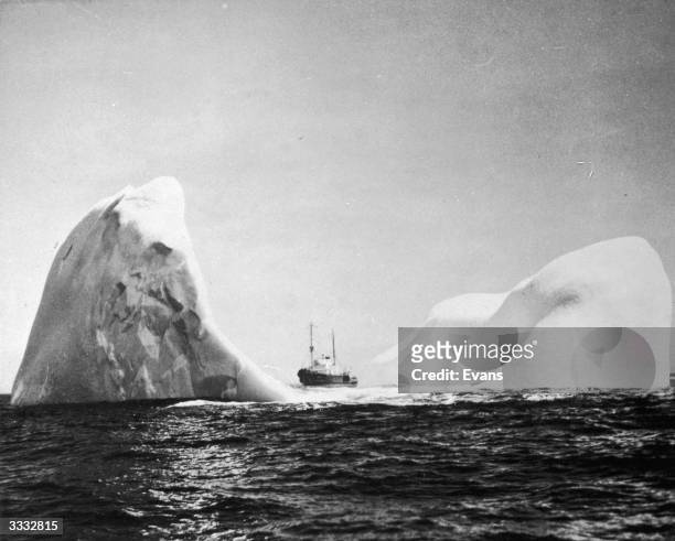 Coast Guard cutter 'Acushnet' dwarfed by a crescent shaped iceberg which rises more than 200 ft above the sea. As 85% of the berg is below the water...