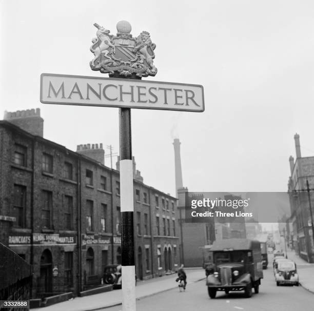 Small textile factories in a street in Manchester, and a road sign with the city's name and crest.