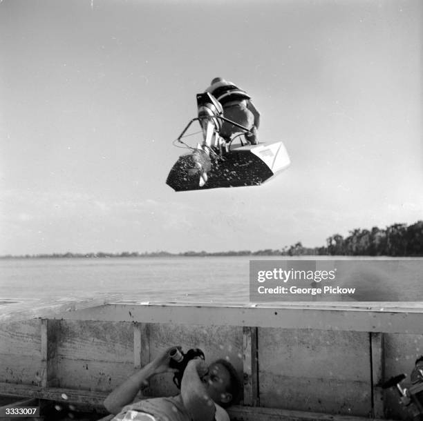 Photographer lies in the bottom of his boat in order to capture an action shot of a speedboat flying overhead, at the Cypress Gardens race course,...