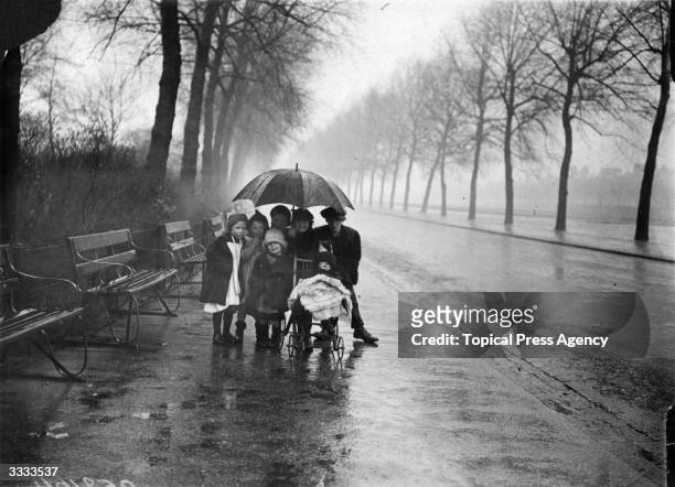 Group of children huddle under a large umbrella, to shelter from the spring rain, in Finsbury Park, London.