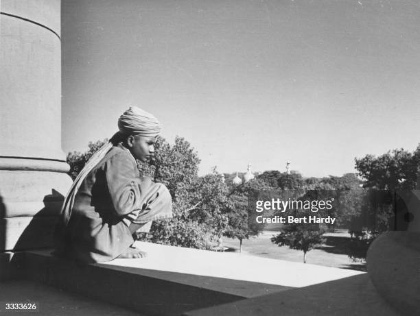 Young boy employed to carry messages around the council house at New Delhi, seat of the Constituent Assembly, sitting in the sun. Original...