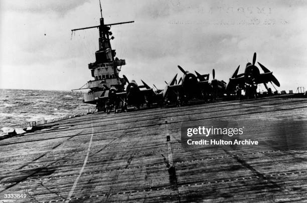 An US aircraft carrier rolling in the heavy seas carrying its cargo of fighter planes against the Japanese. Amongst the planes on board are Avengers...