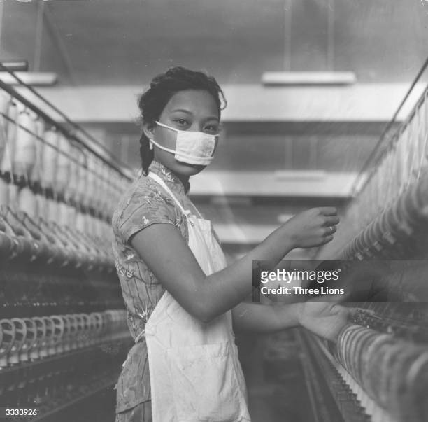 Worker wearing a protective face mask while operating machinery at Nanyang cotton spinning and weaving mill in Hong Kong.
