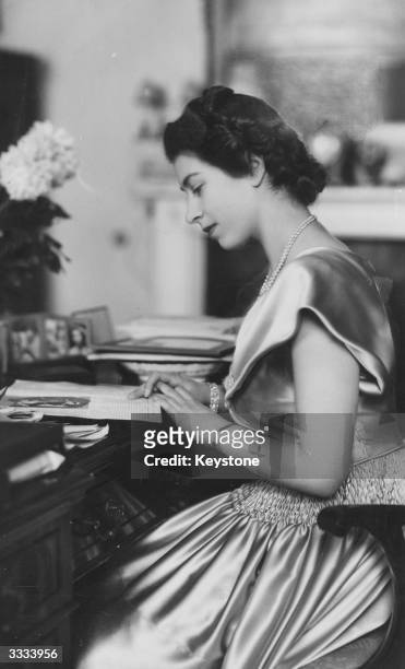 Princess Elizabeth wearing a satin dress at her desk in Buckingham Palace.