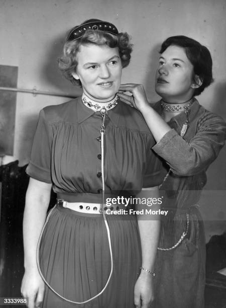 Valerie Davis of Chelsea, London, secures the dog collar around the neck of her friend Peggy Appleton, who wears two more canine contraptions; one as...