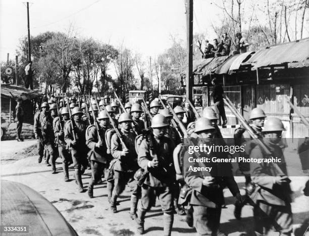 Japanese troops marching past a British post.