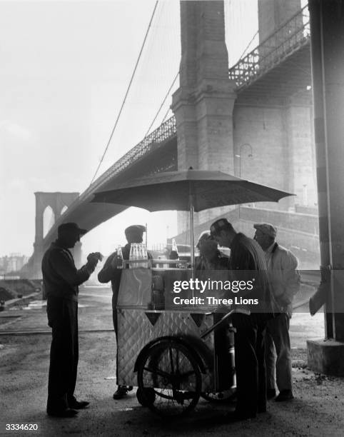 Group of workers getting refreshments from a portable snack stand underneath Brooklyn Bridge, New York, USA.