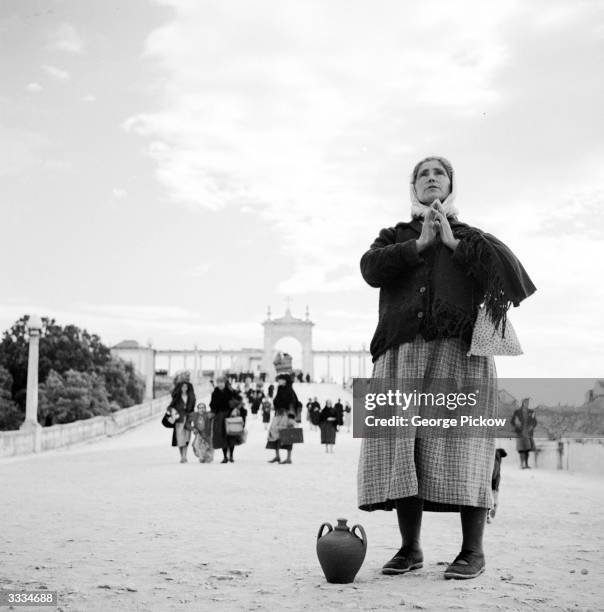 Through the arch leading to the Basilica at Fatima in Portugal, a pilgrim, with her own jug of water to be blessed, makes her devotions. Behind,...