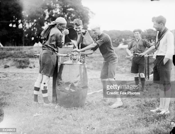 Scouts pouring water over the head of another member sitting in a barrel at the World Jamboree Camp at Birkenhead.