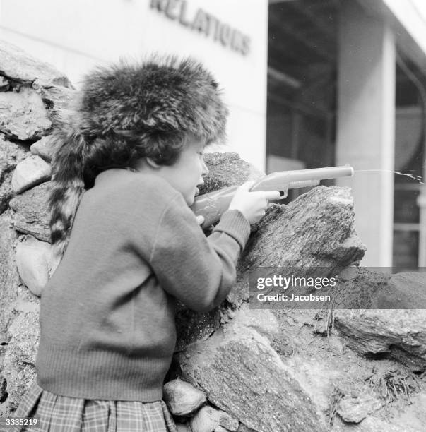 Six year old Susie Jacobsen from New York plays cowboys and indians with a water pistol, dressed in her Davy Crockett hat.