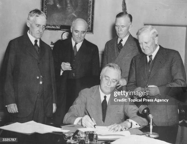 American President Franklin Delano Roosevelt signs the Conscription Bill at the White House. Gathered around him are Secretary of War Henry Stimson ,...