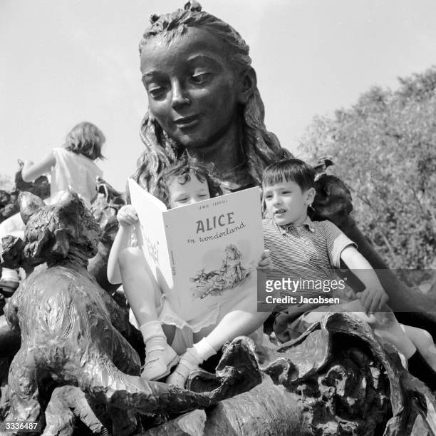 Two children read 'Alice In Wonderland' on Jose de Creeft's statue of Alice in Central Park, New York City, circa 1960.