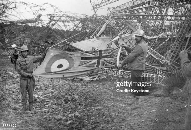 Two French firemen holding a tattered Royal Airforce flag in front of the wreckage of the R101 airship after her crash at 02.08 hours on 5th October...