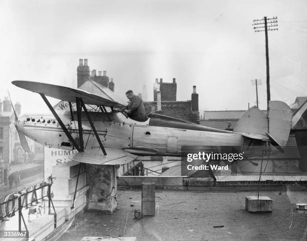 Man cleaning an old Hawker Fury aeroplane that is fixed to the roof of a garage in Gloucester, Gloucestershire.