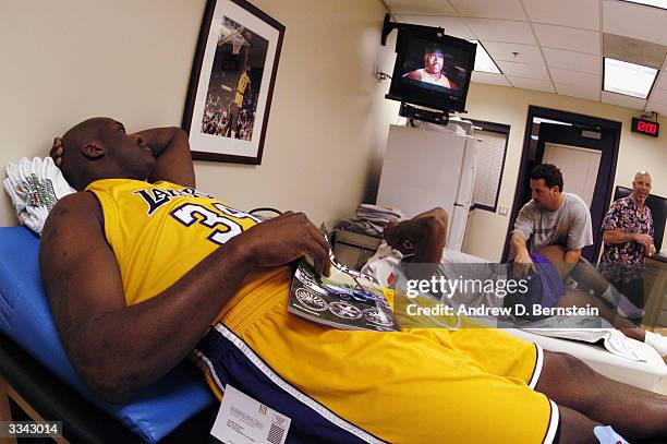 Shaquille O'Neal of the Los Angeles Lakers watches himself on television as he takes a break from reading a magazine while he lays on a trainer's...