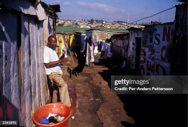 Man smokes a cigarette early in the morning outside his house on February 28, 2004 in Chris Hani, a poor squatter camp in Soweto outside...