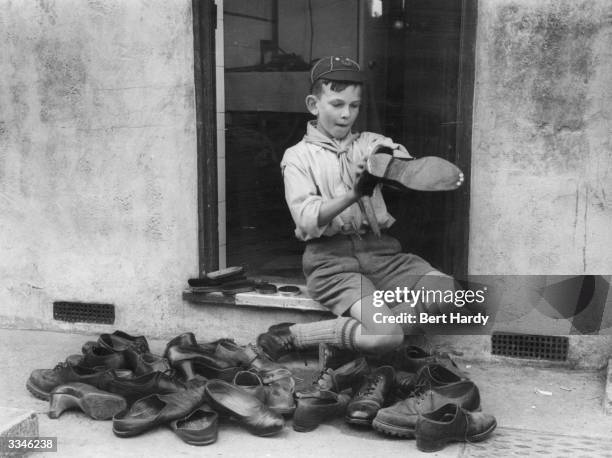 Boy scout of the 7th Royal Eltham Troop earning money for the Boy Scout Association by cleaning shoes and charging a shilling a time. Original...