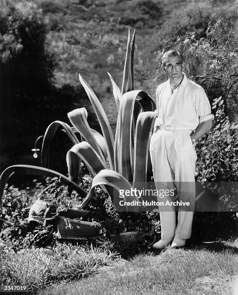 British actor, Boris Karloff standing next to a large cactus plant in ...