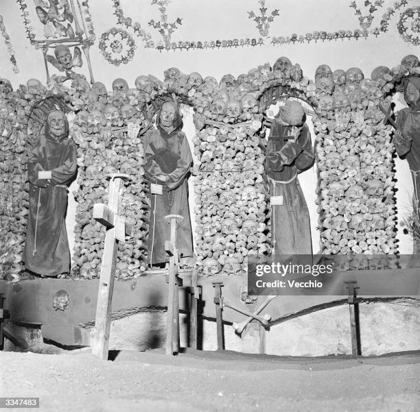 Collection of human skulls and bones surround the hooded, cloaked skeletons of monks in the catacombs of a Capuchin monastery in Rome, In the...