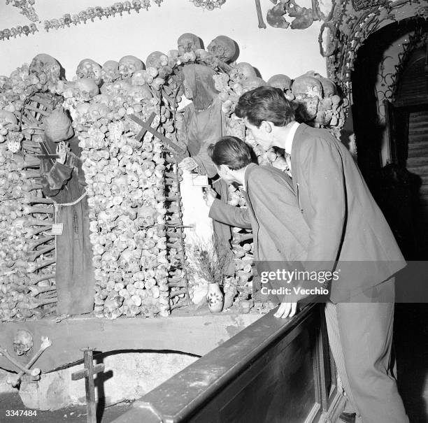 Tourists in the catacombs of a Capuchin monastery in Rome looking at the collection of monk bones and skulls.